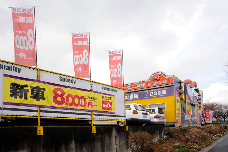 道路側面に大きくもろコミを宣伝！店舗の青い外壁にはカーコン車検も対応していること大きく掲げています！